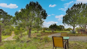 Un espace extérieur aménagé avec deux chaises et une table, entouré d’arbres et bordé d’un chemin de gravier.