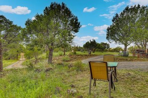 Un espace extérieur aménagé avec deux chaises et une table, entouré d’arbres et bordé d’un chemin de gravier.