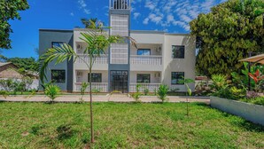 Un edificio moderno de dos plantas con techo plano, varios balcones y un césped cuidado con árboles jóvenes.