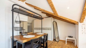 Un coin repas comprenant une table en bois, deux chaises, un présentoir en métal avec des paniers et un banc blanc.