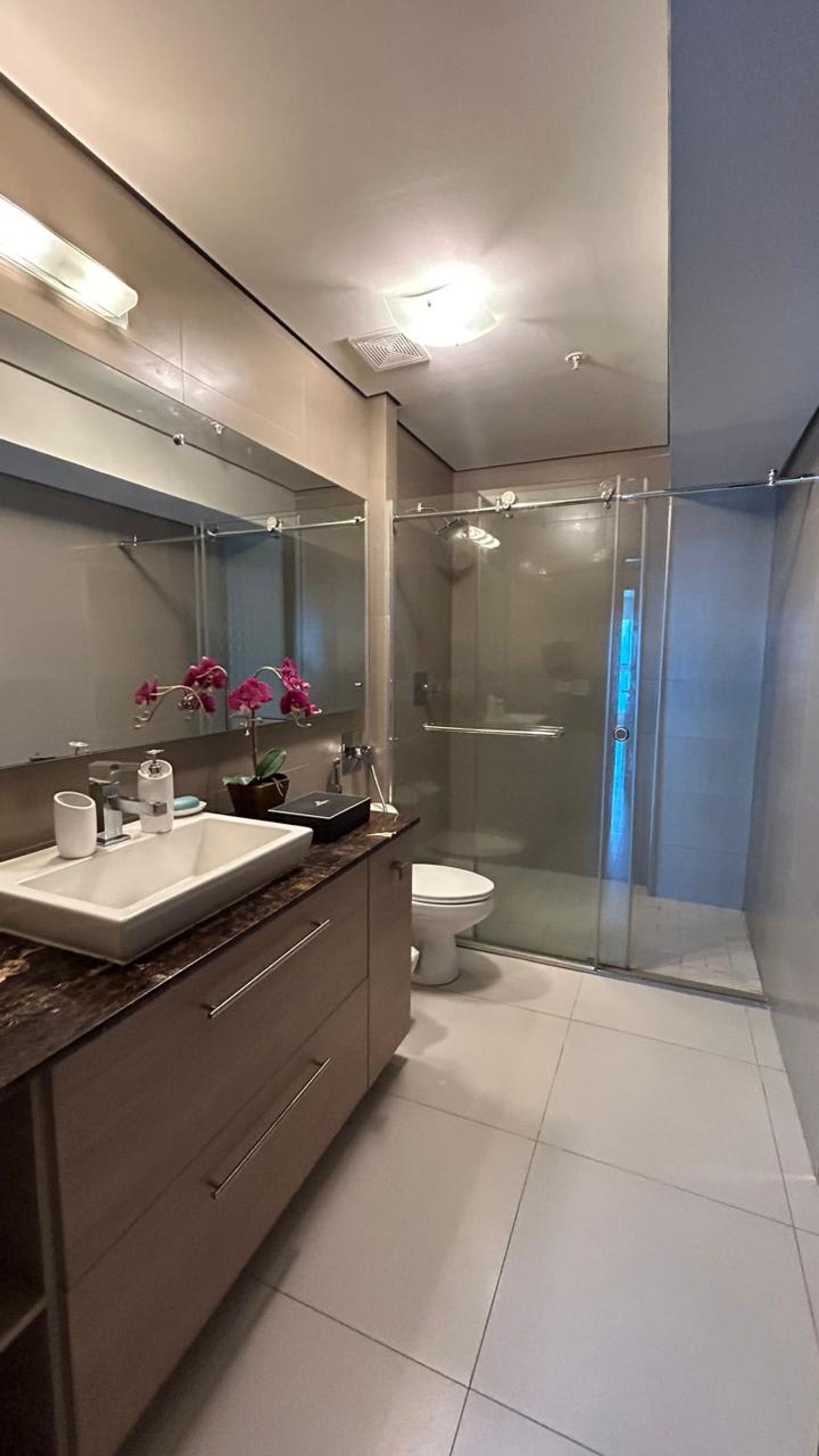 Une salle de bain moderne avec une douche à l’italienne en verre, un lavabo blanc et un meuble-lavabo avec des tiroirs.