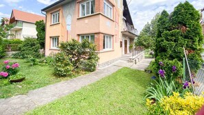Una casa a due piani con un portico anteriore, un piccolo giardino fiorito e un vialetto lastricato.