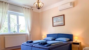 Ein Schlafzimmer mit Bett, Nachttisch, Stuhl, einem Fenster mit Vorhängen, einer Heizung und einem Bild an der Wand.