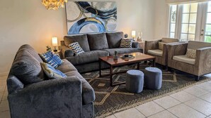 A modern living room with a grey sofa, a coffee table, and a patterned rug. There is a ceiling fan and a large abstract painting on the wall.