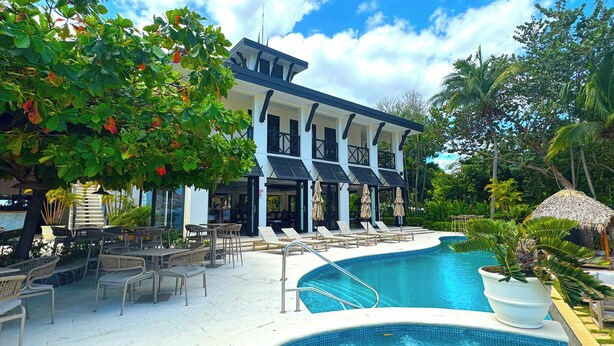 A two-story building with a pool area, outdoor seating, and lush greenery.