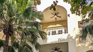 A multi-story building with a central balcony, a garage, and surrounding greenery.