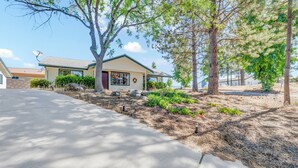 A residential house with a driveway, a satellite dish, and a well-maintained lawn with trees and shrubs. - Modern Mountain Calm – Oakhurst Home by Yosemite (Oakhurst)