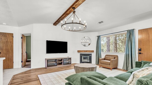 A spacious living room with a large green sofa set, a wooden coffee table, a fireplace, and a television mounted on the wall. - Modern Mountain Calm – Oakhurst Home by Yosemite (Oakhurst)