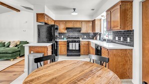 A modern kitchen with wooden cabinets, a black refrigerator, and a tiled backsplash. - Modern Mountain Calm – Oakhurst Home by Yosemite (Oakhurst)