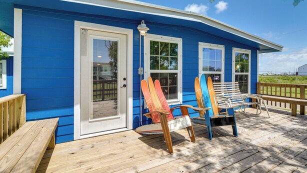 Ein blaues Haus mit einer Holzterrasse, zwei Adirondack-Stühlen und einer Bank.