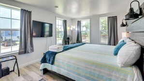 Ein Schlafzimmer mit einem großen Bett, einem flachbildfernseher an der Wand und mehreren Fenstern mit Vorhängen.