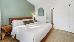 A bedroom with a large bed, a nightstand, a lamp, a mirror, and a door. - Yosemite Getaway! Stylish 2BR near south gate (Oakhurst)