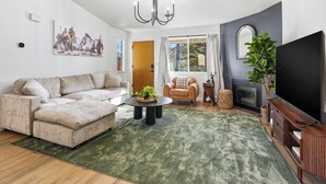 A modern living room with a sectional sofa, a round coffee table, a fireplace, and a large TV. - Yosemite Getaway! Stylish 2BR near south gate (Oakhurst)
