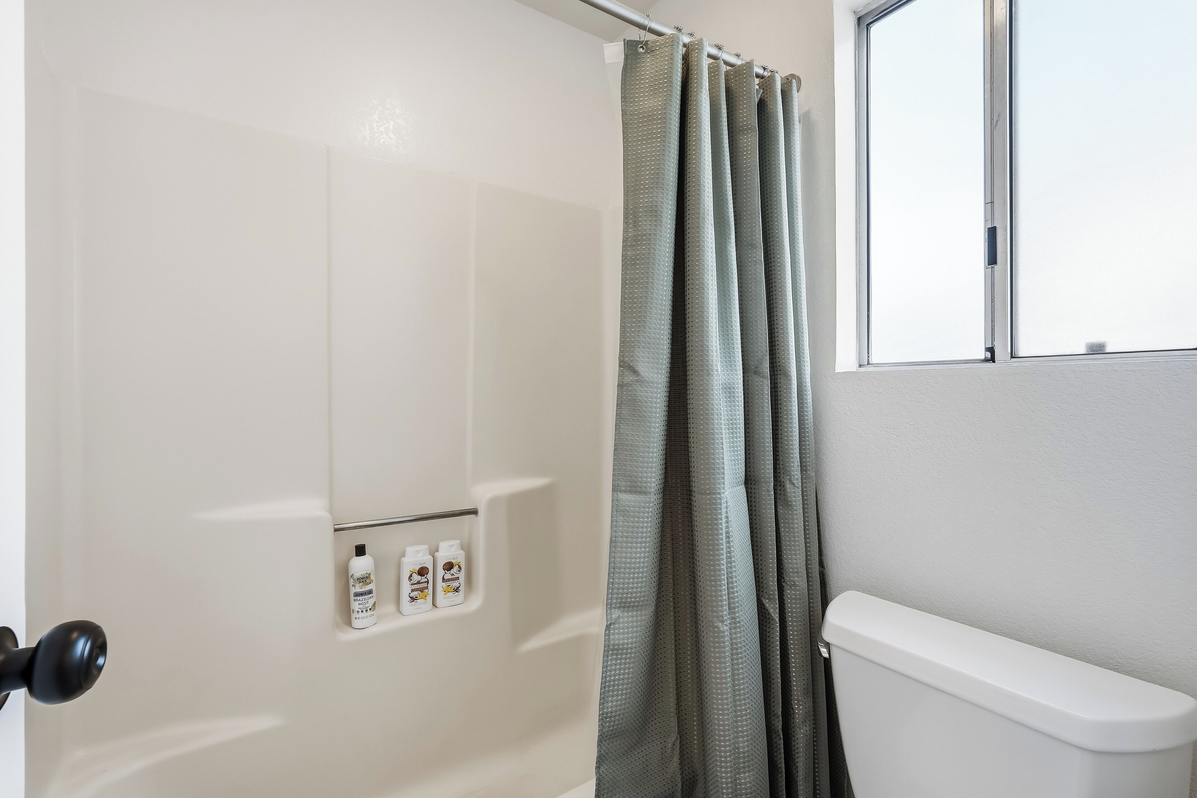 Une salle de bain avec un rideau de douche, des toilettes et une fenêtre.