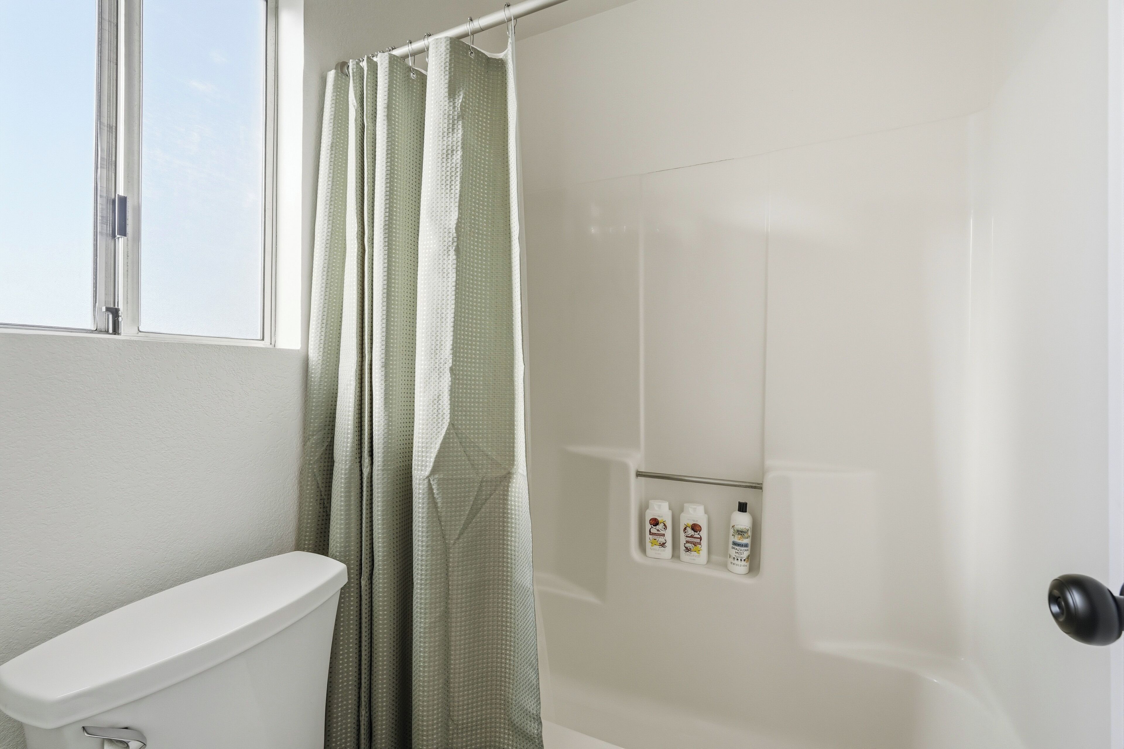 Un baño con inodoro, cortina de ducha y dispensador de jabón en la pared.