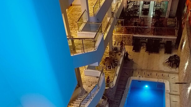 Et hotel med flere etager, central swimmingpool, udendørs siddeområder og udsigt til poolen fra de øverste etager.