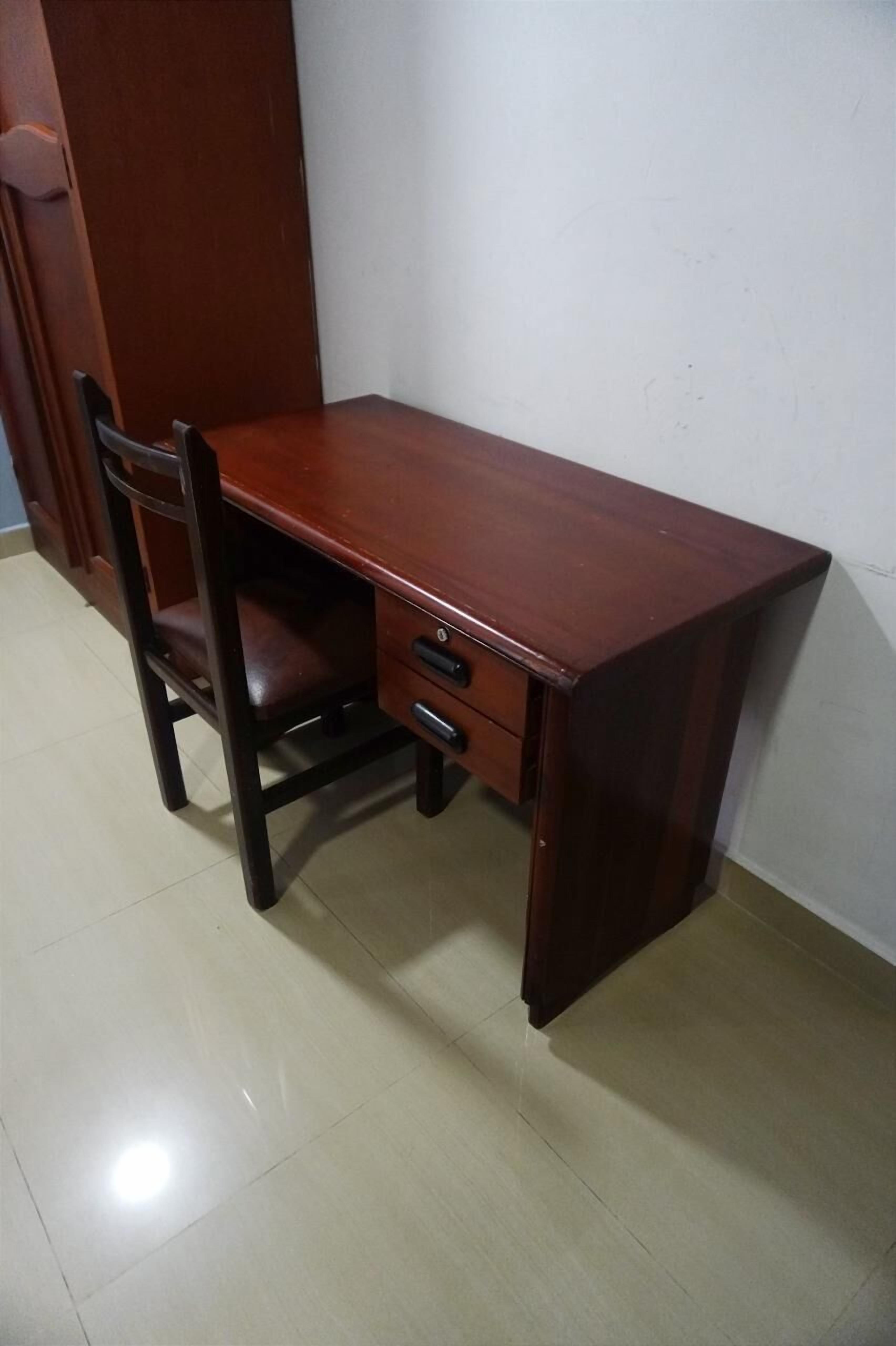 Un escritorio de madera con una silla, un cajón y un armario frente a una pared lisa.