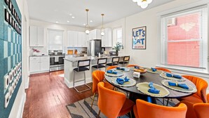 A modern kitchen with white cabinets, a central island, and orange chairs around a dining table.