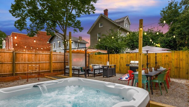 A backyard with a hot tub, outdoor seating, and a wooden fence.