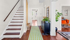 A staircase with wooden steps and a white wall, leading to a hallway with a checkered rug, a dark blue console, and a potted plant.