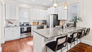 A modern kitchen with white cabinets, stainless steel appliances, a granite countertop, and bar seating.