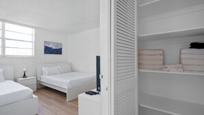 A bedroom with a bed, bedside tables, a TV, and a closet with folded towels. - Condo w/2 Queen beds and Ocean View | Tides (Hollywood)