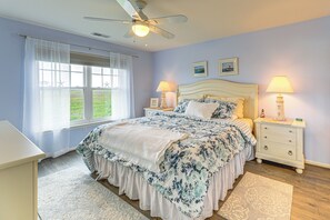 Ein Schlafzimmer mit einem Bett, zwei Nachttischen mit Lampen, einem Deckenventilator und einem Fenster mit Vorhängen.