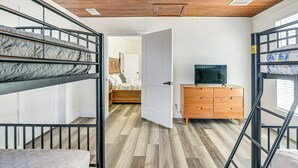 A room with bunk beds, a wooden dresser, a television, and a door leading to another room. - Close to Beach: Walkable Galveston Getaway! (Galveston)