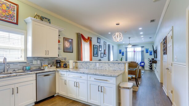 A modern kitchen with white cabinetry, a granite countertop, and a wooden floor. - Family Home w/ Fenced Backyard in New Orleans! (New Orleans)