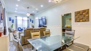 A modern living room with a glass dining table, comfortable seating, a flat-screen TV, and decorative wall art. - Family Home w/ Fenced Backyard in New Orleans! (New Orleans)