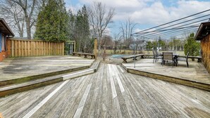 A wooden deck with a pool table, outdoor seating, and a view of the surrounding area including trees and a building. - Deck & Seasonal Pool: Spacious Home Near Buffalo! (Buffalo)