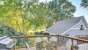 A wooden deck with a glass table and wicker chairs, surrounded by trees. - Walk to Spring Lake w/ Waterpark: Family Retreat! (North Mankato)