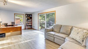 A spacious living room with a wooden floor, a beige sofa, a wooden desk, and a bookshelf. - Walk to Spring Lake w/ Waterpark: Family Retreat! (North Mankato)