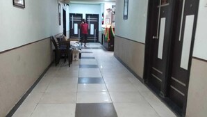 A corridor with tiled flooring, a bench, and a door with a sign. - Ppmotel alibag  (Alibag)