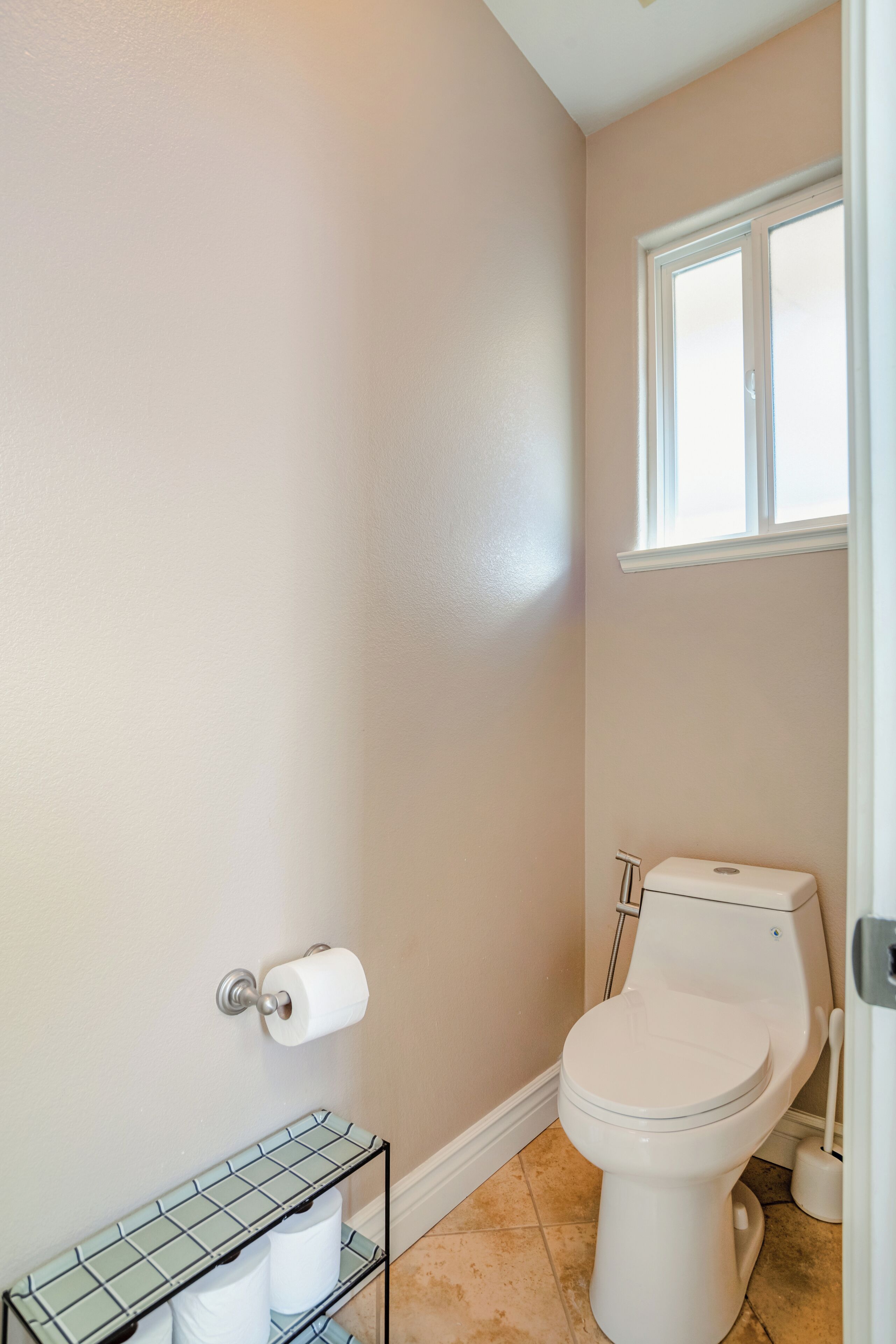 A bathroom with a toilet, a roll of toilet paper on the wall, and a shelf with two rolls.