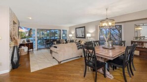 Amplia sala de estar con una mesa de comedor de madera, asientos cómodos y grandes ventanales que ofrecen vistas al exterior.