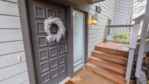 Puerta principal con corona decorativa, buzón y escalera de madera que lleva a un porche.