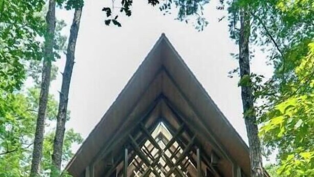 Un edificio con techo triangular y una entrada central, rodeado de árboles.