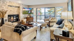 Un salón espacioso con chimenea de piedra, asientos cómodos y grandes ventanales que ofrecen vistas al exterior.