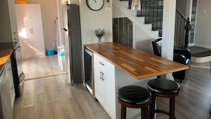Una cocina con una isla de madera, armarios blancos, un refrigerador de acero inoxidable y un reloj en la pared.