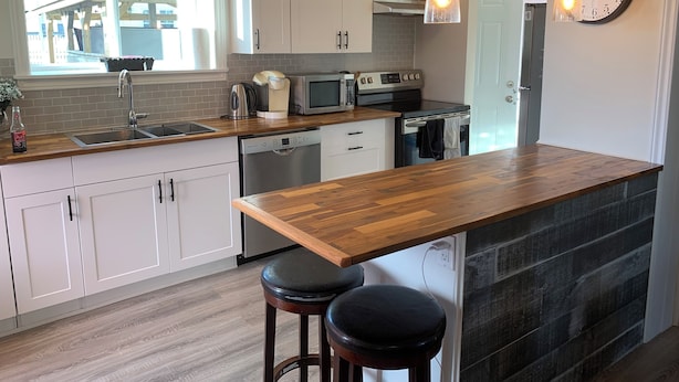 Una cocina moderna con armarios blancos, encimera de madera, horno empotrado y un reloj de pared.