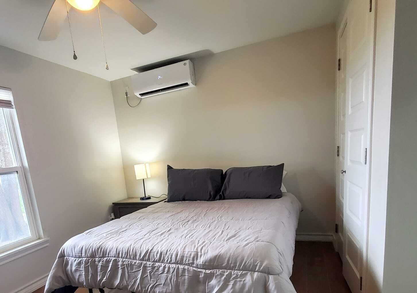 Een slaapkamer met een bed, nachtkastje, lamp, airconditioner en plafondventilator.