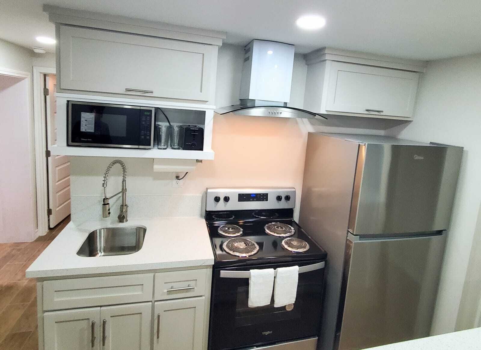 A compact kitchen with white cabinets, a stainless steel refrigerator, a black stove with four burners, and a microwave above the sink.