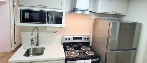 A compact kitchen with white cabinets, a stainless steel refrigerator, a black stove with four burners, and a microwave above the sink.
