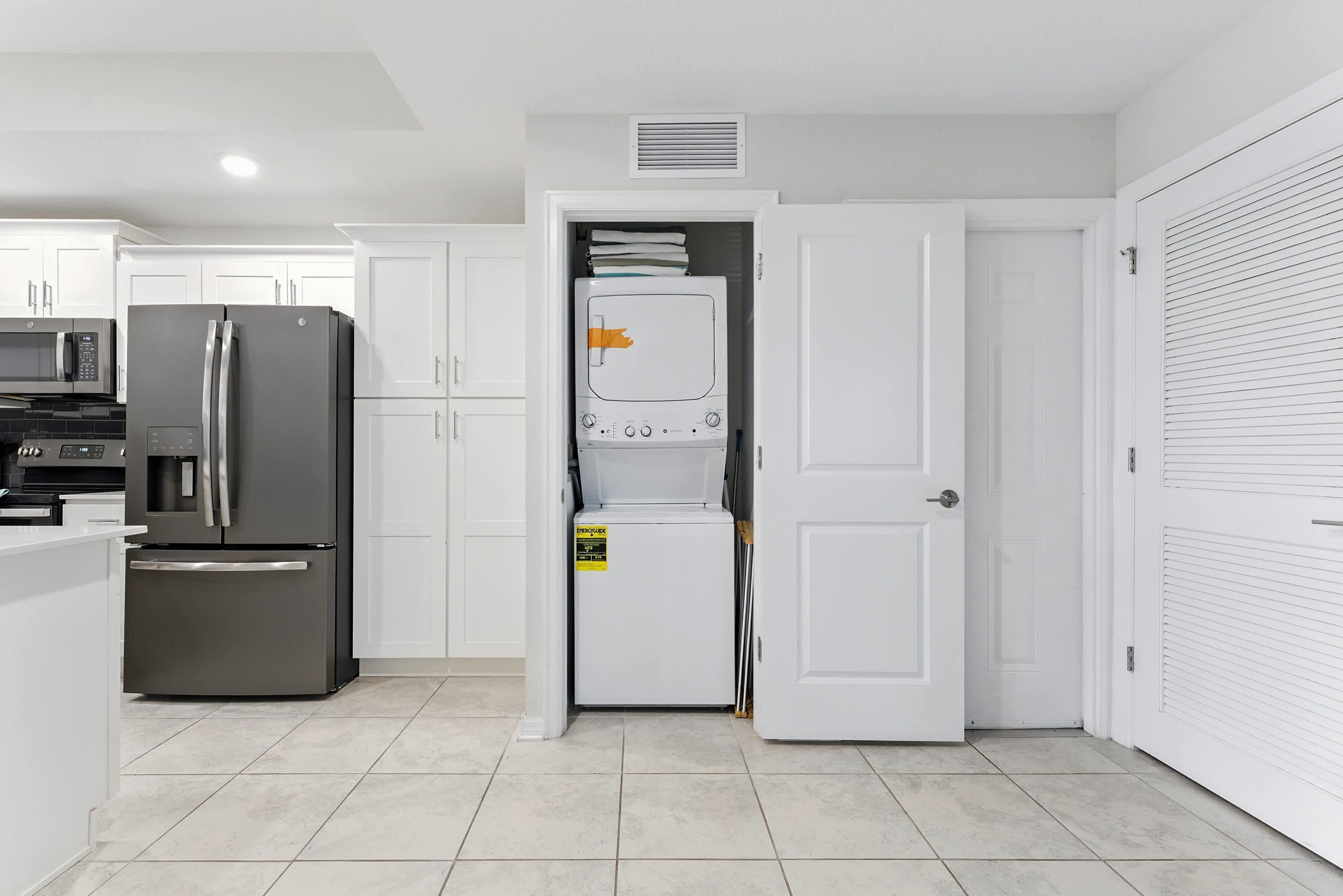 A modern kitchen with white cabinetry, a stainless steel refrigerator, and a microwave.