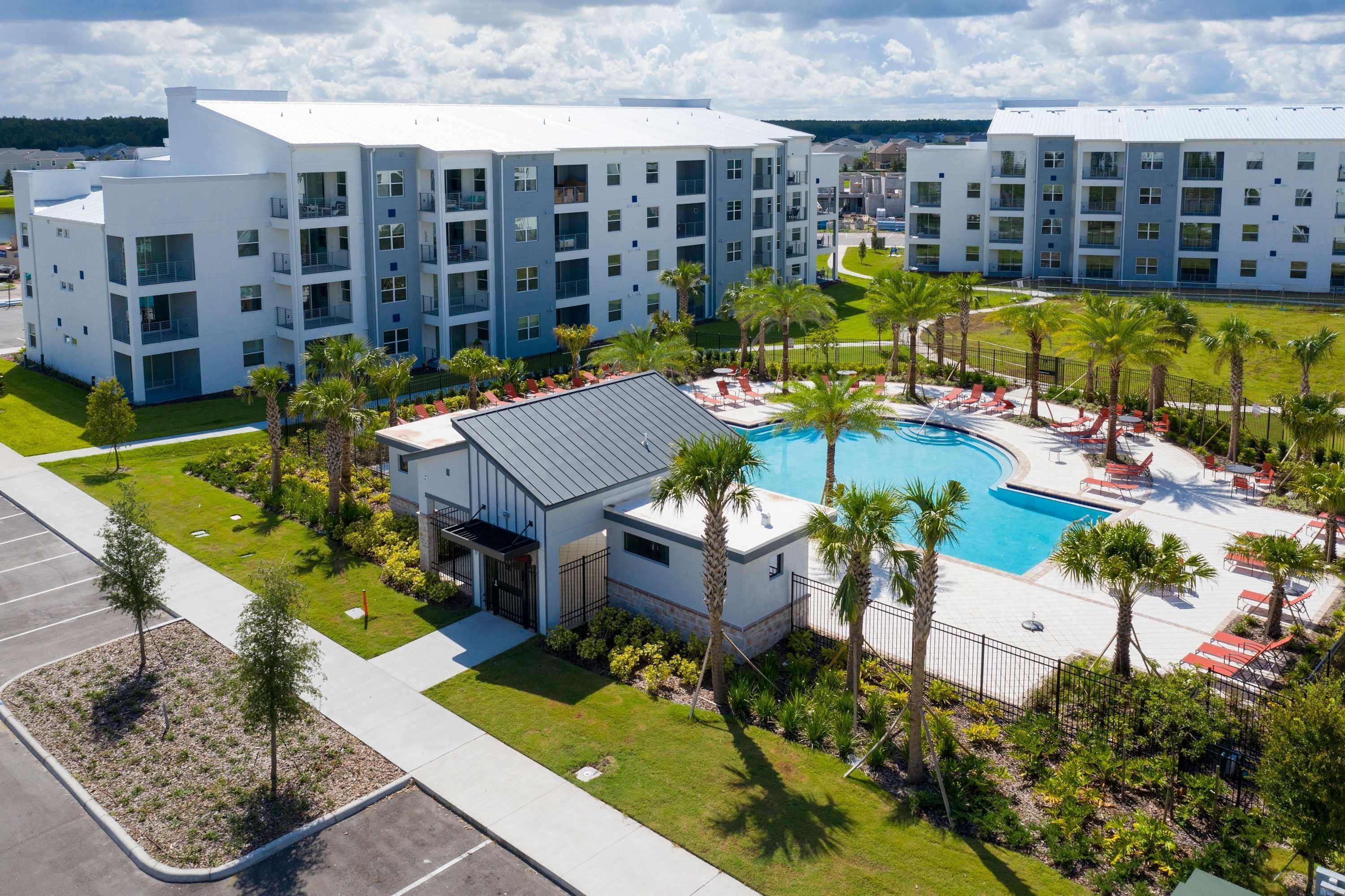 A modern hotel with a swimming pool surrounded by palm trees and lounge chairs.