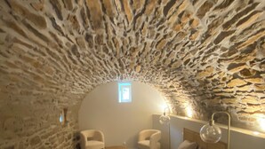 Un dormitorio acogedor con paredes de piedra, una cama, dos sillones, una mesita de noche y un ventanal.