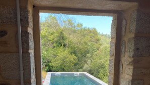 An outdoor swimming pool with a stone wall and pebbles leading to it, surrounded by greenery.