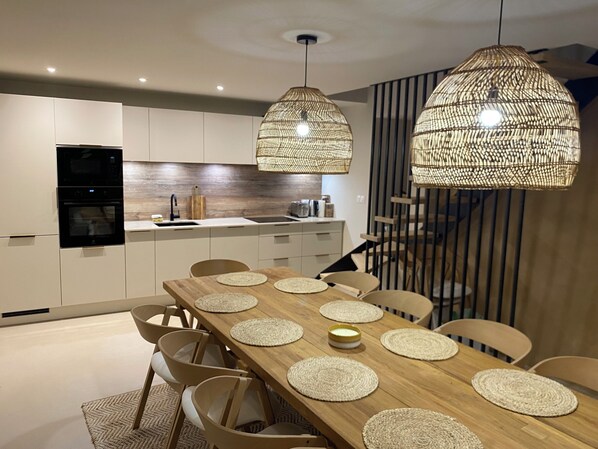 A modern kitchen with white cabinets, a black oven, and a wooden dining table with placemats.