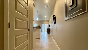 Un pasillo con una puerta a la izquierda, una zona de cocina al fondo y un cuadro en la pared.